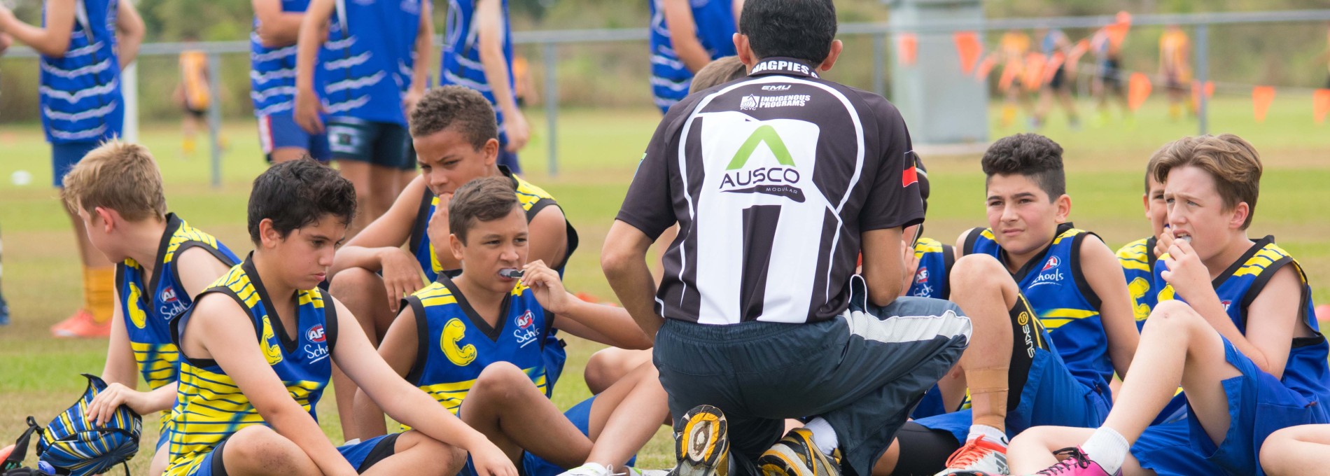 A Young Male AFL team on sports grounds with coach speaking